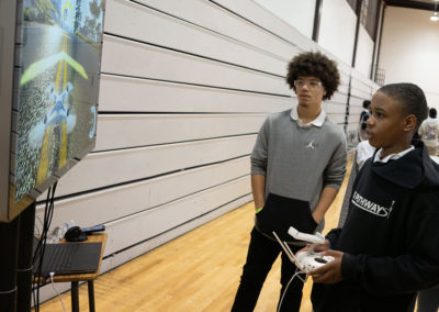 Two students playing a drone videogame on a TV screen