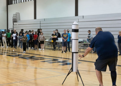 A group of students watching a presenter explain the rules at the drone competition